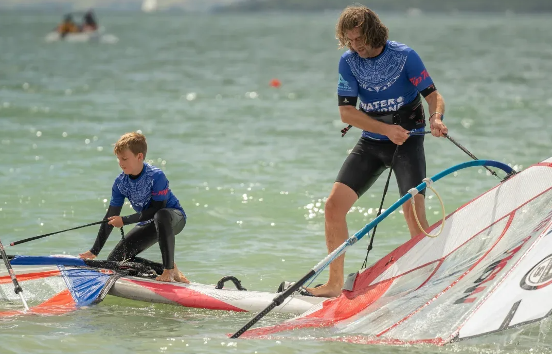Instructor teaching a child balance and sail position in shallow water
